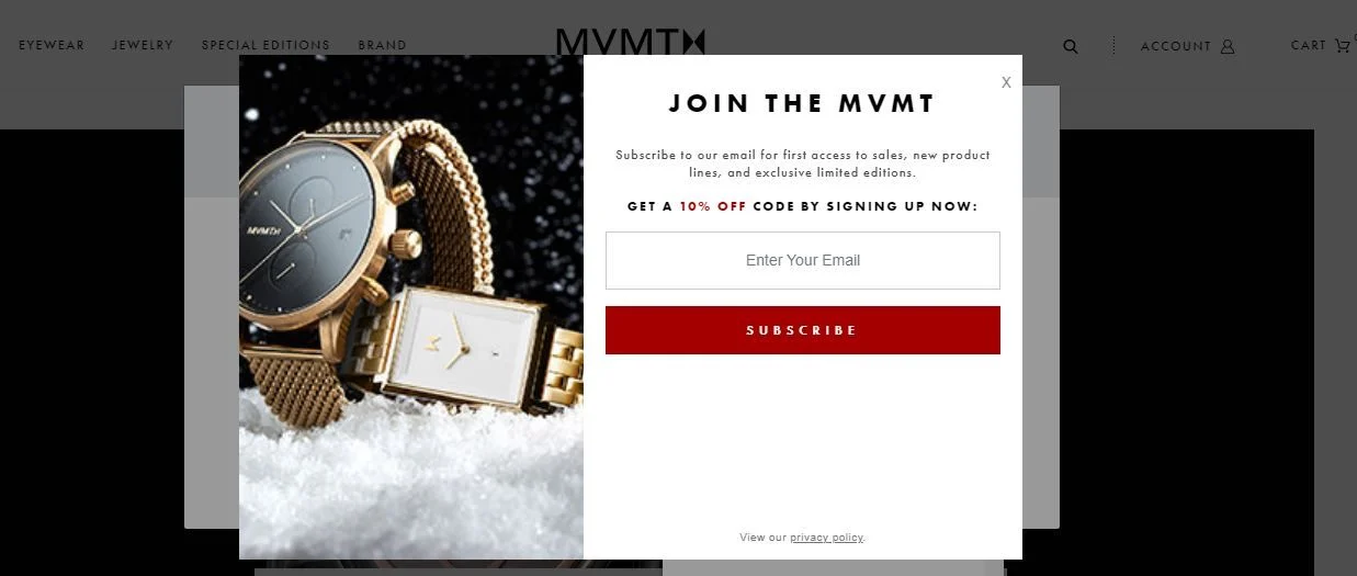 A gold wristwatch with a dark face is displayed on a snowy surface, with text inviting viewers to subscribe to The MVMT email for exclusive offers.