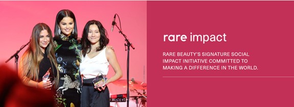 Three women standing together at a microphone against a pink background, next to text reading "rare impact" describing Rare Beauty's social impact initiative committed to making a difference in the world.